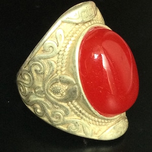 May include: A silver ring with an ornate design and a large, oval-shaped red gemstone.