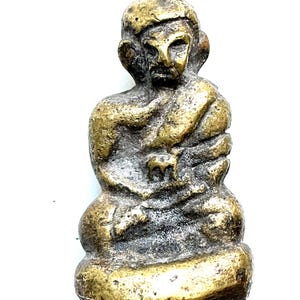 May include: A small, antique-looking bronze figurine of a seated figure with a serene expression. The figure is wearing a robe and has a detailed face and head covering. The bronze has a weathered appearance.