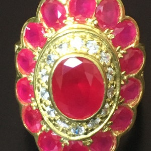 Op de afbeelding: Een gouden ring met een grote rode robijn omringd door kleinere rode robijnen en witte diamanten.