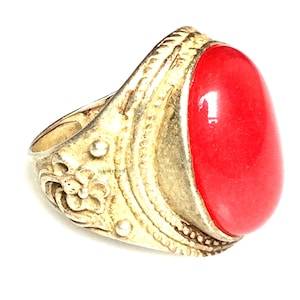 Puede incluir: Anillo antiguo de tono dorado con una gran piedra roja de forma ovalada. El anillo tiene detalles intrincados alrededor de la banda y el engaste, con una superficie texturizada. El anillo es probablemente vintage o de inspiración vintage.