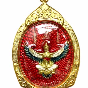 May include: Gold-colored pendant with an oval, red center featuring a detailed image of a mythical bird with outstretched wings. The pendant has intricate gold filigree around the edges and a small loop for a chain.