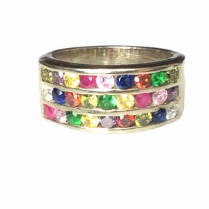 May include: A silver ring with three rows of colorful gemstones. The gemstones are in various colors, including red, pink, yellow, green, and blue. The ring is a band style.