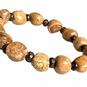 May include: A beaded bracelet featuring light brown, irregularly shaped beads interspersed with small, dark brown beads. The bracelet is made of natural materials and has a neutral color palette.