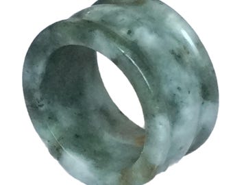 May include: A green jade ring with white and brown marbling. The ring is thick and has a rounded shape.