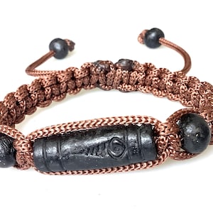 Peut inclure: Bracelet en macramé marron avec une perle cylindrique noire centrale et des perles sphériques noires. Le bracelet présente un design tissé et une fermeture réglable. Un bijou unique.