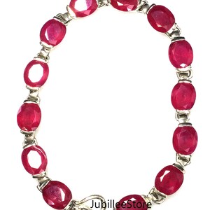May include: A silver bracelet featuring oval-cut, deep red gemstones. The gemstones are linked together with silver connectors and secured with a hook clasp. The bracelet is displayed against a white background. The text "JubileeStore" is visible.
