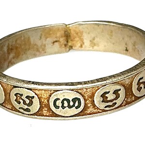 Op de afbeelding: Een zilveren ring met een band van kleine, cirkelvormige ontwerpen. Elke cirkel bevat een donker, gestileerd symbool. De ring heeft een versleten, antieke uitstraling, met een aangetaste, goudbruine band. De ring staat tegen een witte achtergrond.