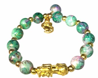 May include: A beaded bracelet featuring green and purple marbled beads with gold accents. The bracelet includes two gold-colored charm pieces, one at the clasp and one in the center.
