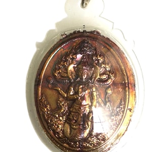 May include: A gold-toned metal pendant featuring a detailed depiction of a deity with multiple arms, holding a sphere in one hand. The pendant is encased in a clear plastic oval frame.