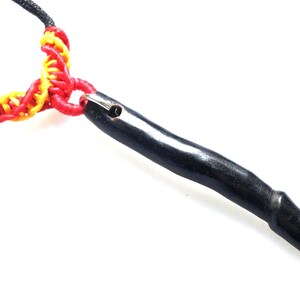 Può includere: Collana nera con un ciondolo in legno nero. La collana è realizzata con un cordoncino intrecciato rosso e giallo.