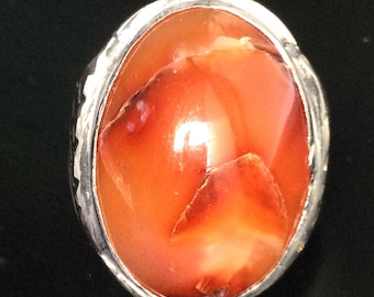 May include: A silver ring with a large, oval-shaped carnelian stone. The stone is a deep orange color with white and brown veins.