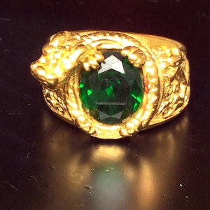 Op de afbeelding: Een gouden ring met een groene edelsteen in een drakenontwerp.