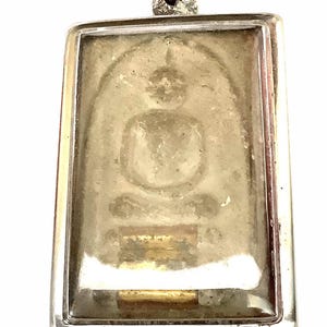 May include: A rectangular silver pendant with a detailed image of a seated Buddha figure. The pendant has a clear, protective cover over the image, and is attached to a silver chain.