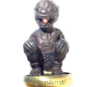 May include: A dark grey figurine of a seated, humanoid creature with a single red eye. The figure has a textured surface and is sitting on a gold-coloured base with text. The figurine is set against a white background.