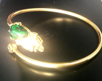 May include: A gold bangle bracelet with a green gemstone and a detailed animal design.