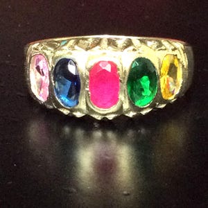 May include: A gold ring set with five oval-shaped gemstones. The gemstones are pink, blue, red, green, and yellow.