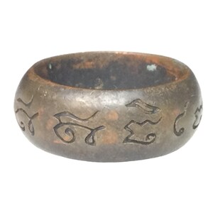 May include: A dark brown metal ring with intricate carvings on the outside. The carvings appear to be ancient symbols or letters.