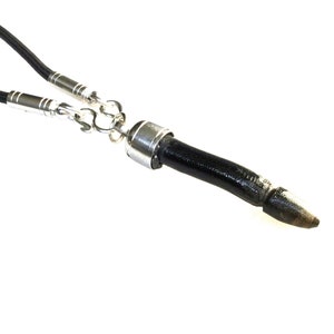 Può includere: Una collana in pelle nera con un ciondolo in argento a forma di punta. Il ciondolo ha un anello in argento nella parte superiore e un cordino in pelle nera attaccato ad esso.