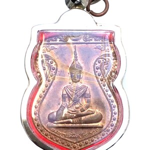 Könnte beinhalten: Ein silberner und goldener Anhänger mit einem Buddha-Bild in einem durchsichtigen Plastikgehäuse mit rotem Rand. Der Anhänger hat eine silberne Schlaufe zum Aufhängen.