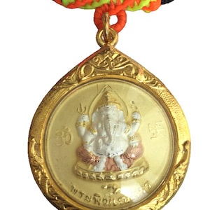May include: A gold-colored pendant necklace featuring a detailed image of a deity with a white body, gold crown, and pink accents. The pendant is suspended from a black cord with a decorative orange and green knot.