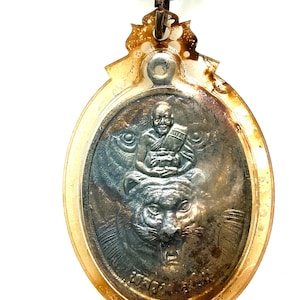 Op de afbeelding: Zilveren hanger met een gedetailleerde afbeelding van een zittende figuur boven een tijgerkop. De hanger heeft een helder, ovaalvormig frame met een decoratieve bovenkant en een zilveren ketting.