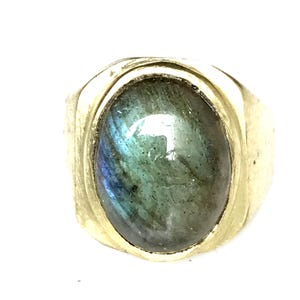 Puede incluir: Un anillo de oro con una gran piedra ovalada de labradorita. La piedra preciosa tiene un brillo verde, azul e iridiscente.