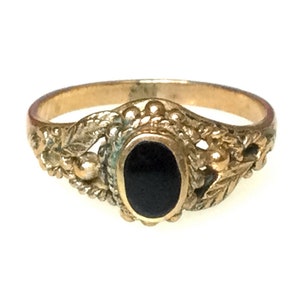 May include: A vintage gold ring with an oval black stone. The ring has detailed floral and leaf patterns around the stone and on the band. The design is classic and ornate, with a slightly aged appearance.