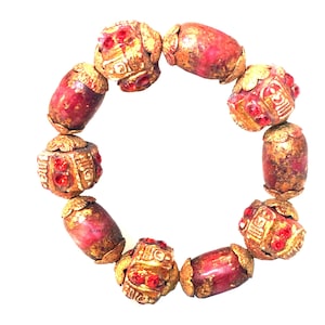 May include: A red and gold beaded bracelet. The bracelet features a series of red, barrel-shaped beads interspersed with ornate gold-colored beads. The gold beads have red accents. The bracelet is displayed on a white background.