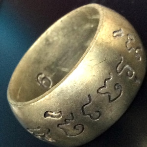 Op de afbeelding: Een zilveren ring met ingewikkelde gegraveerde ontwerpen en Thaise tekst.