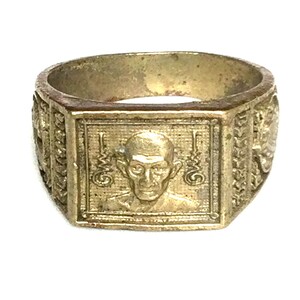 Op de afbeelding: Een vintage goudkleurige ring met een rechthoekige voorkant met een gedetailleerd portret. De band van de ring heeft ingewikkelde reliëfpatronen aan de zijkanten. De ring is waarschijnlijk gemaakt van een metaallegering.