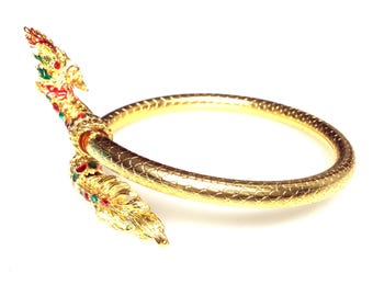 Könnte beinhalten: Ein goldenes Armreif-Armband mit einem Drachenkopf-Design. Der Drache ist mit roten, grünen und blauen Edelsteinen verziert.