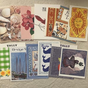 May include: A collection of vintage greeting cards with various designs. The cards feature images of seashells, flowers, birds, sailboats, and abstract patterns. Some cards have the word "TALLY" printed on them.