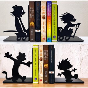 May include: A set of black metal bookends featuring silhouettes of a boy and a tiger character. The top set shows the characters in a wagon, while the bottom set depicts them in dynamic poses. These bookends support a row of various hardcover books.