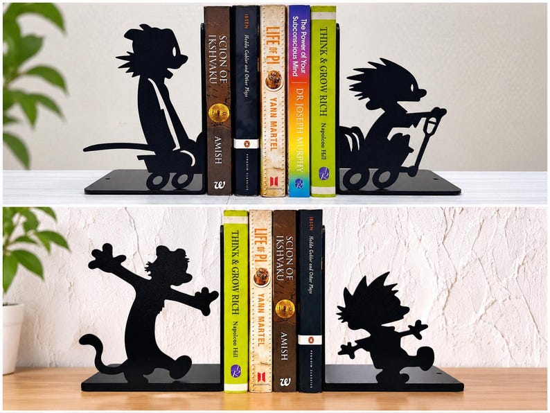 May include: A set of black metal bookends featuring silhouettes of a boy and a tiger character. The top set shows the characters in a wagon, while the bottom set depicts them in dynamic poses. These bookends support a row of various hardcover books.