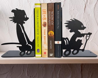 May include: A pair of black metal bookends featuring silhouettes of a character pulling a wagon and a character riding in a wagon. The bookends support four books titled Think & Grow Rich, Life of Pi, Scion of Ikshvaku, and Hedda Gabler and Other Plays.