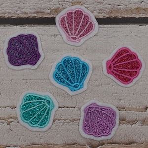 Könnte beinhalten: Sechs bunte Muschel-Patches in Lila, Rosa, Türkis und Blau mit glitzernden Details und weißen Rändern. Diese gestickten Patches eignen sich perfekt, um Kleidung oder Accessoires einen Hauch von Meer zu verleihen.