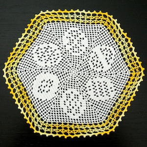 Può includere: Un centrino bianco all'uncinetto con un bordo giallo e arancione. Il centrino ha una forma esagonale e un motivo a spirale al centro.