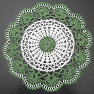 May include: A round, handmade crochet doily featuring a central sage green circle surrounded by a white, intricate, openwork lace pattern, finished with a wide, scalloped sage green border with small white picot edge details.