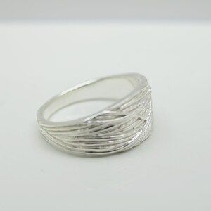 Könnte beinhalten: Ein silberner Ring mit einem strukturierten, gewebten Design. Der Ring ist breit und hat eine abgerundete Form.