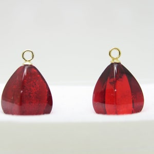 Op de afbeelding: Twee rode glazen hangers in druppelvorm met gouden springringen. De hangers hebben een getextureerd, facetgeslepen uiterlijk.