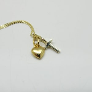 May include: A gold chain necklace with a small gold heart charm and a silver cross charm.