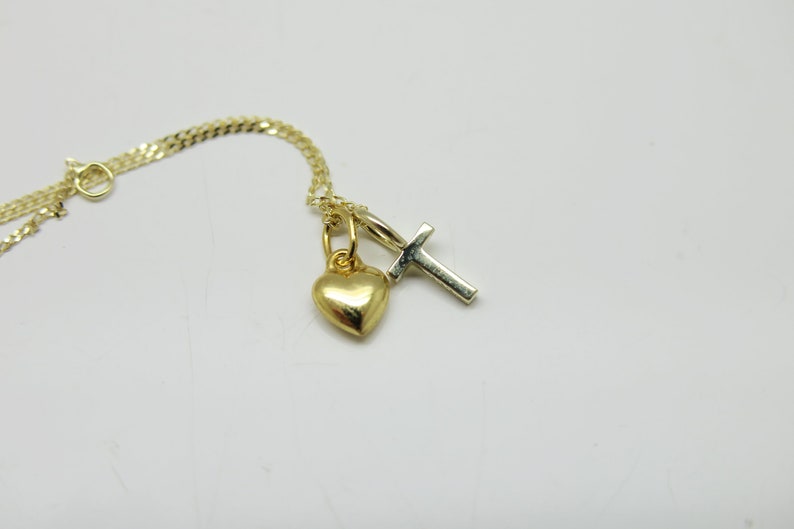 May include: A gold chain necklace with a small gold heart charm and a silver cross charm.