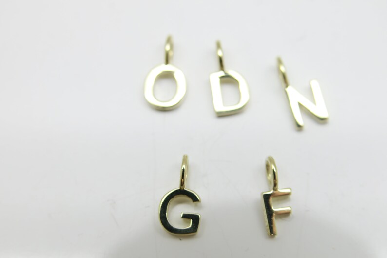 May include: Six gold-colored metal letter charms, each with a loop for attaching to a necklace or bracelet. The letters are O, D, N, G, and F.