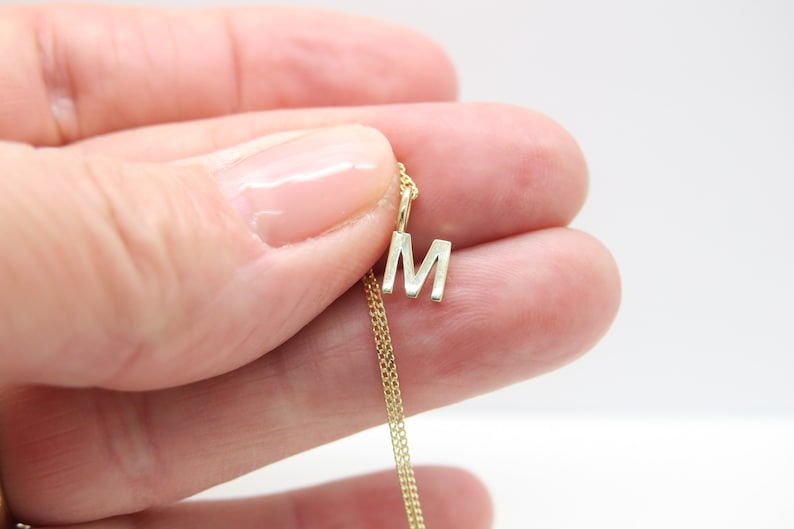 May include: A gold chain necklace with a small, silver letter 'M' pendant.