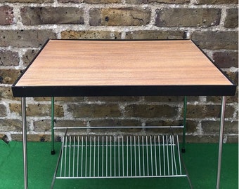 May include: A mid-century modern side table with a wood top and black trim. The table has a chrome wire shelf underneath.