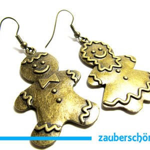 Könnte beinhalten: Ein Paar goldfarbene Lebkuchenmann-Ohrringe. Die Ohrringe sind aus Metall und haben ein detailliertes Lebkuchenmann-Design.