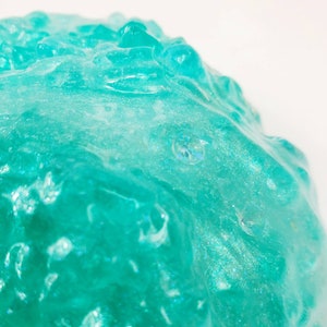 May include: Close-up of a teal blue slime with a glittery texture. The slime is smooth and appears to be very soft.
