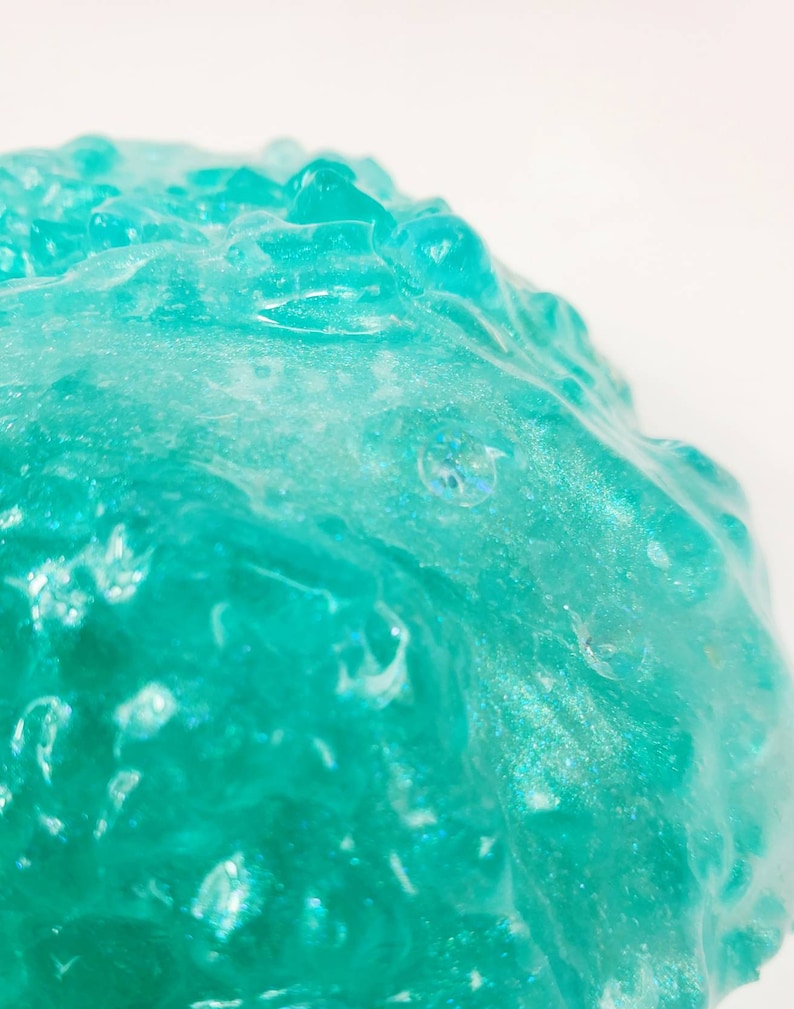 May include: Close-up of a teal blue slime with a glittery texture. The slime is smooth and appears to be very soft.
