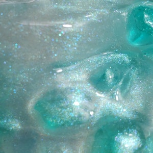 May include: Close-up of a translucent teal blue slime with iridescent glitter. The slime has a textured, bubbly surface.