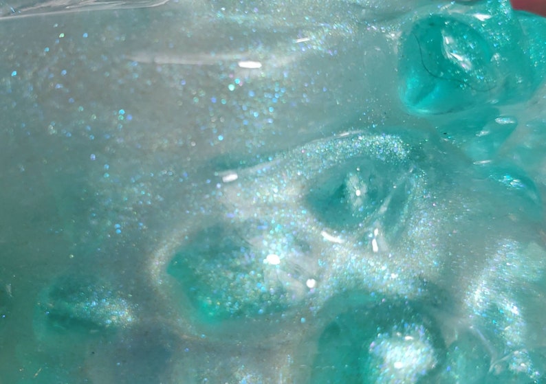 May include: Close-up of a translucent teal blue slime with iridescent glitter. The slime has a textured, bubbly surface.